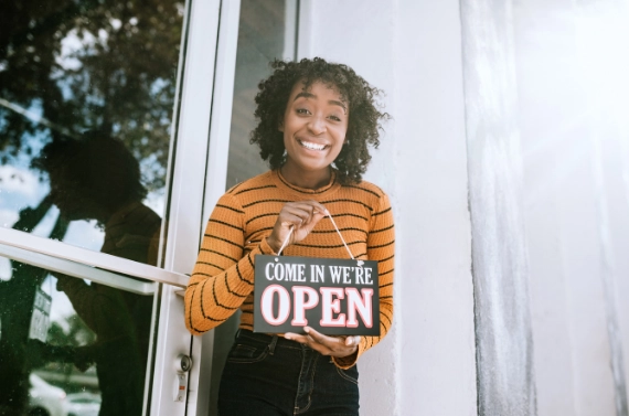 Small business owner standing at storefront holding an open sign.